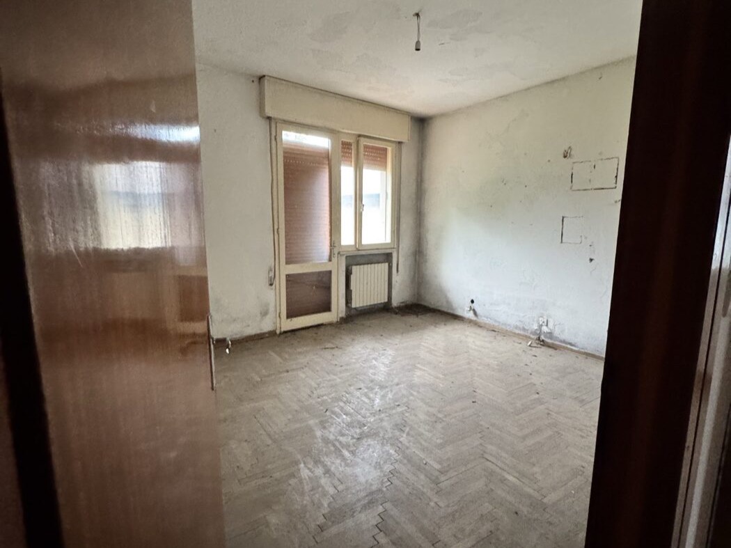 Camera prima della ristrutturazione: parquet a spina rovinato e muri con rappezzi